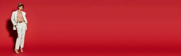 A young, handsome man stands confidently, showcasing a modern look with a bold red backdrop. — Stock Photo