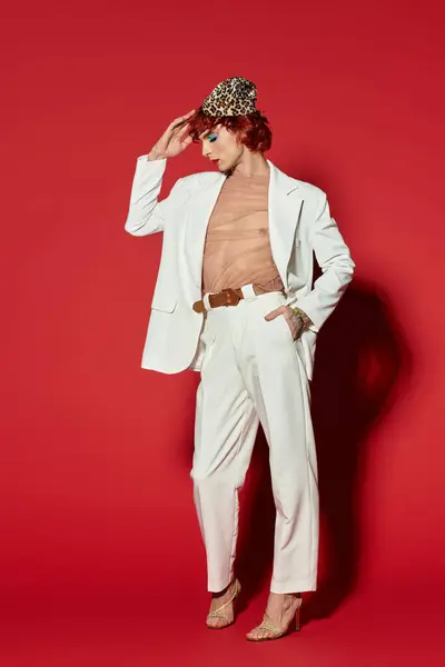 A young man confidently poses in a striking white suit against a red background. — Stock Photo