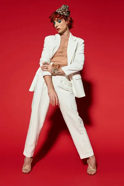A young man with a striking appearance showcases a stunning white suit on a bold red background. — Stock Photo