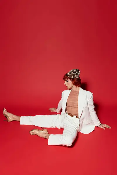 A young man with unique style lounges effortlessly on a striking red backdrop, exuding confidence. — Stock Photo