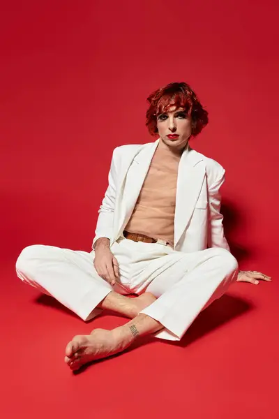 A young man sits against a vibrant red backdrop, showcasing his unique style. — Stock Photo