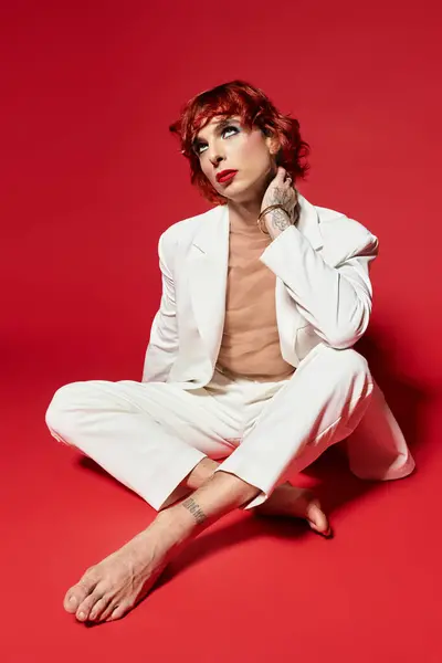 A unique young man showcases his bold fashion choice in a white suit against a vibrant red backdrop. — Stock Photo