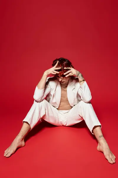 Sitting with a thoughtful pose, a handsome young man contrasts against a bold red backdrop. — Stock Photo