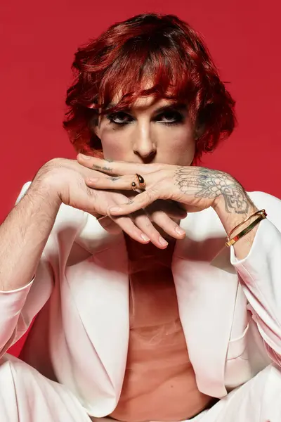 A handsome young man with vibrant red hair sits thoughtfully against a bold red backdrop. — Stock Photo