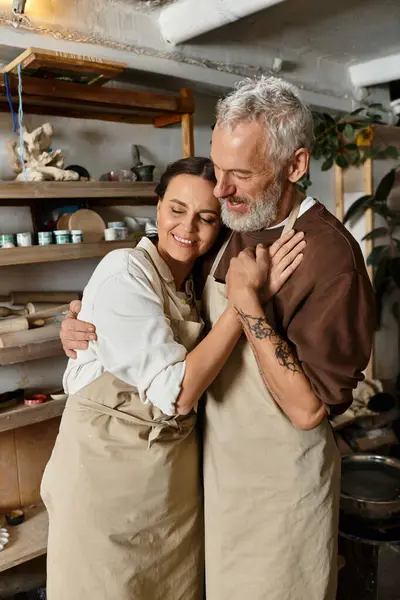 Mature couple shares quality time in a pottery class, shaping clay and embracing each other warmly. — Stock Photo