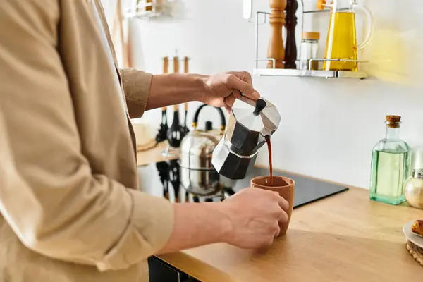 Un joven con ropa casual vierte café en una taza, saboreando la mañana en casa. - foto de stock