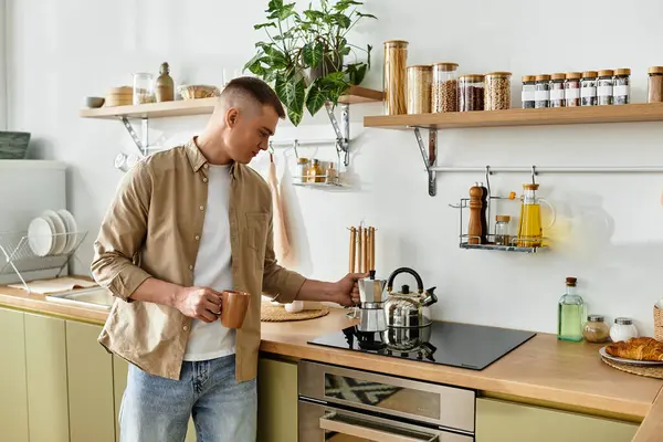 A young man in casual attire happily makes coffee while surrounded by modern kitchen decor. — Stock Photo