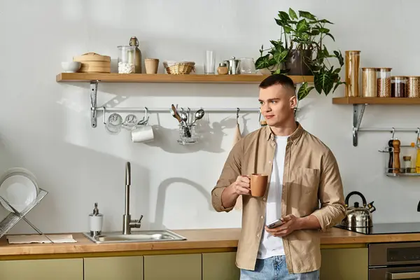 Handsome young man dressed casually savors a drink while standing in his modern kitchen. — Stock Photo
