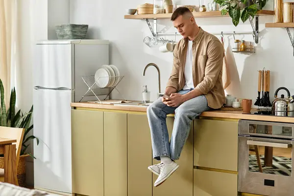 Handsome young man relaxes in his modern apartment, lost in thought while sitting on the counter. — Stock Photo