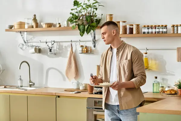 Ein junger Mann in lässiger Kleidung steht in einer modernen Küche und genießt seine Mahlzeit und Ruhe. — Stockfoto