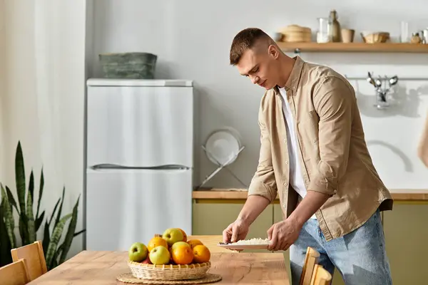 A young man in casual clothes cooks in his stylish kitchen, surrounded by fresh fruits. — Stock Photo