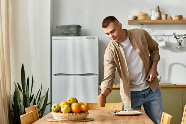 A young man in casual clothes sips a drink at a cozy table filled with fresh fruit and a meal. — Stock Photo