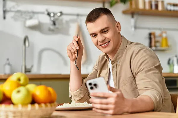 Handsome young man smiles while scrolling on his phone, surrounded by a cozy home atmosphere. — Stock Photo