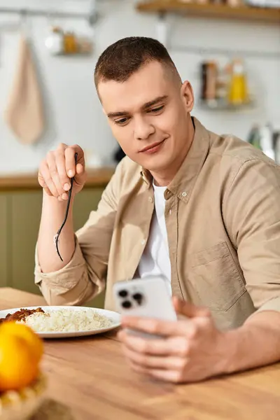 Young man in casual clothes relaxes at his modern apartment, enjoying food and using his phone. — Stock Photo