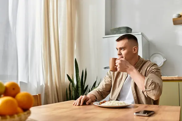 A young man in casual clothes sips his drink while enjoying breakfast in a stylish apartment. — Stock Photo