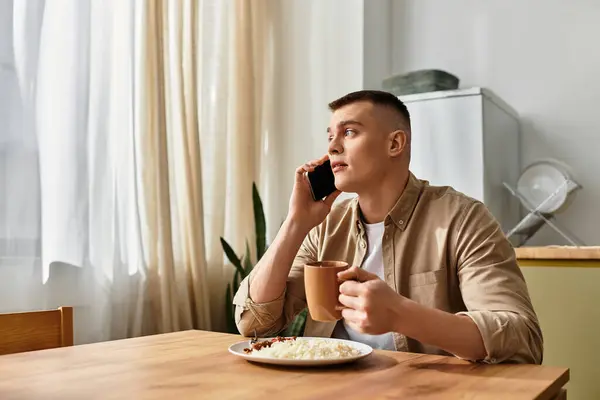 Молодий чоловік співає каву за дерев'яним столом, спілкуючись на телефоні в сучасній обстановці. — Stock Photo