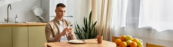 In a bright modern apartment, a young man relaxes at the table, enjoying moments on his phone, banner — Stock Photo