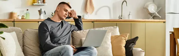 A young man in casual attire is focused on his laptop while relaxing at home, banner — Stock Photo