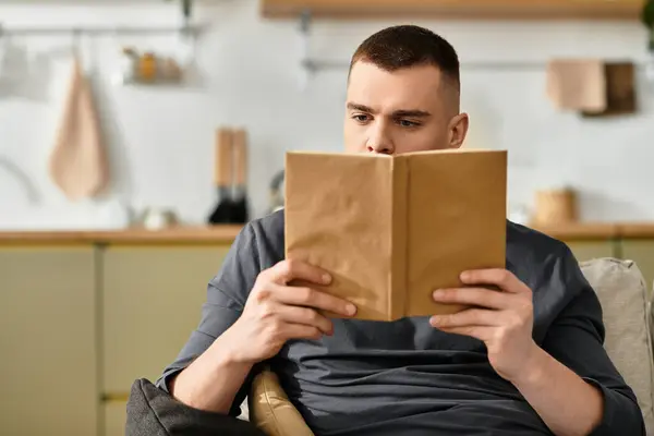 Relaxing at home, a handsome young man reads a book in casual attire, surrounded by modern decor. — Stock Photo
