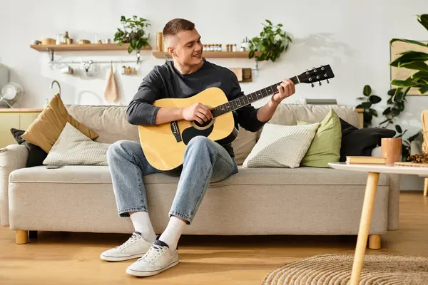 Relaxing in his stylish apartment, a young man strums his guitar, enjoying a cozy afternoon. — Stock Photo