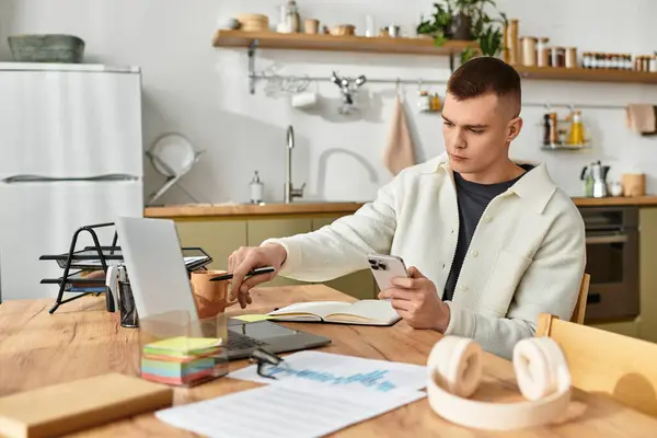 Enfocado joven se dedica a un trabajo remoto desde su cocina moderna, equilibrando las tareas en los dispositivos. — Stock Photo