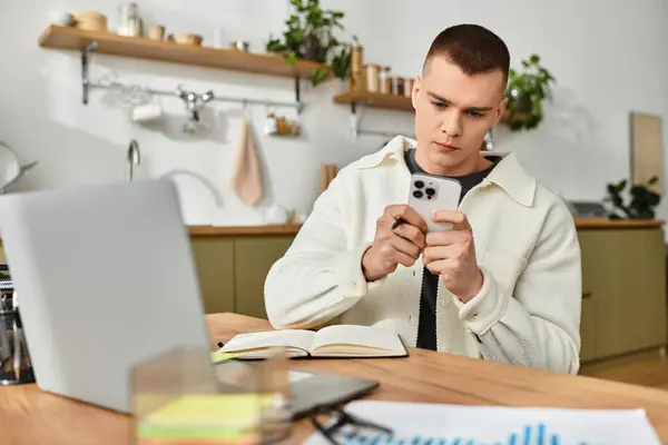 A young man in casual clothes is working on his laptop and phone in his modern apartment. — Stock Photo