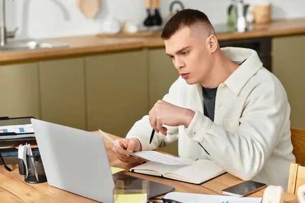 A handsome young man, dressed casually, is intently working at his modern apartment desk. — Stock Photo