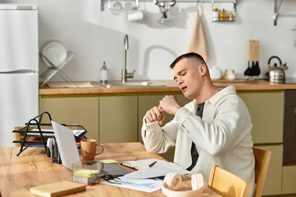 Joven guapo trabajando desde casa en una elegante mesa de cocina mientras toma un descanso. — Stock Photo