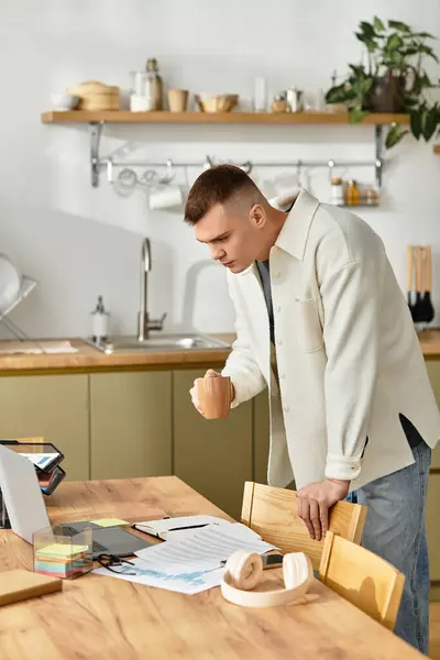Focalisé jeune homme en tenue décontractée fonctionne de la maison tout en sirotant son verre dans une cuisine élégante. — Photo de stock