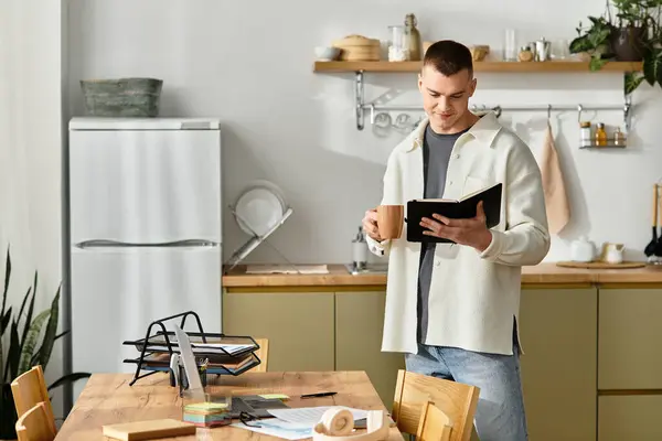 Un giovane uomo in abbigliamento casual sorseggia caffè mentre recensisce le note al suo elegante tavolo da cucina. — Foto stock