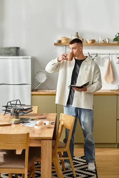 Handsome young man in casual clothes sips coffee while working on a laptop at home. — Stock Photo