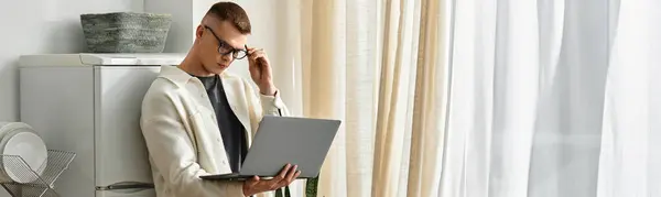 Hombre joven guapo en atuendo casual se involucra en el trabajo remoto de su apartamento moderno, pancarta - foto de stock