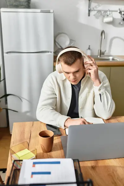 Engaged in remote work, a young man writes notes while focused on his laptop and coffee. — Stock Photo