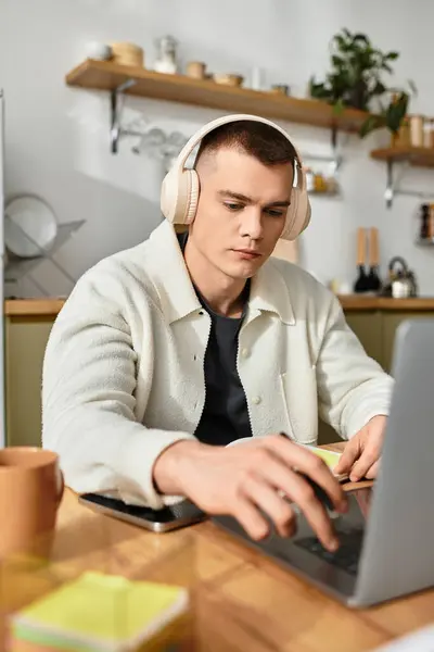 Young man in casual clothes types on his laptop while seated at a stylish wooden desk. — Stock Photo