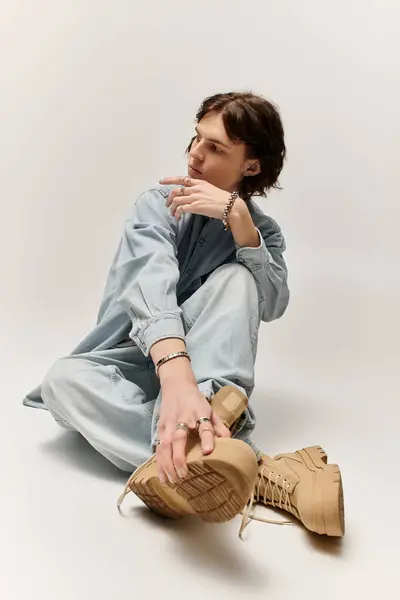 Un joven guapo se sienta en el suelo, irradiando un ambiente relajado y moderno en un estudio sencillo. - foto de stock