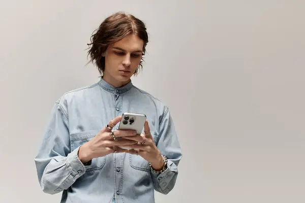 Hombre guapo en camisa de mezclilla centrado en su teléfono inteligente, exudando estilo y confianza. - foto de stock
