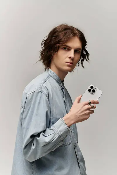 Handsome young man poses with confidence, holding a smartphone against a neutral backdrop. — Stock Photo