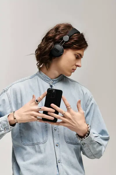 Un jeune homme branché interagit avec son smartphone tout en portant des écouteurs élégants, respirant le charme. — Photo de stock