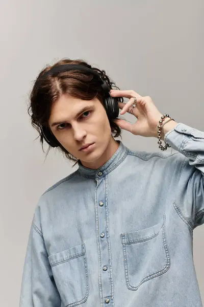 Handsome young man in a denim shirt listens to music with focus and style in a modern setting. — Stock Photo