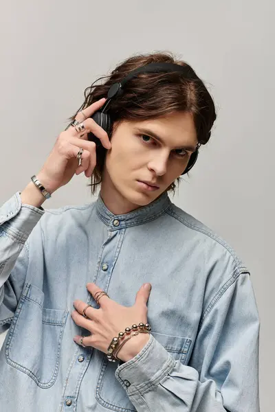 A confident young man in a denim shirt and headphones gestures thoughtfully to the music. — Stock Photo