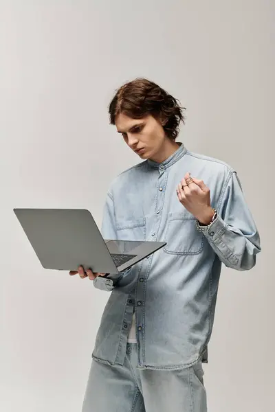A handsome young man dressed in denim engages with his laptop, showcasing his stylish flair. — Stock Photo