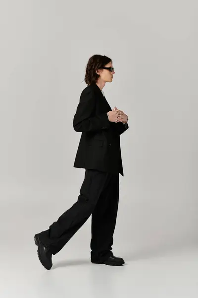 Handsome young man dressed in a sleek black outfit walks gracefully across a light backdrop. — Stock Photo
