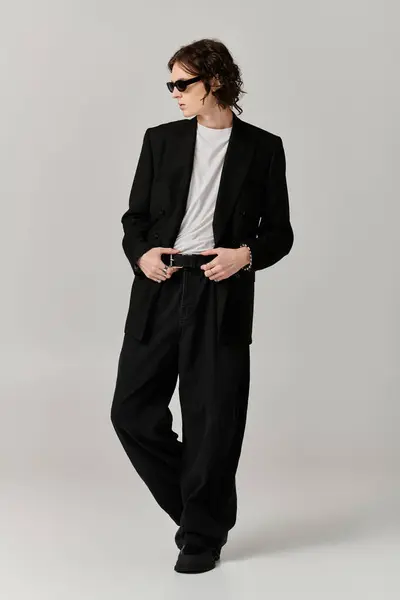 A handsome young man stands confidently, showcasing a chic black outfit in a modern setting. — Stock Photo
