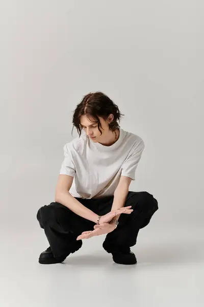 Un jeune homme s'accroupit élégamment dans une tenue chic, exprimant un charme artistique dans un cadre lumineux. — Photo de stock