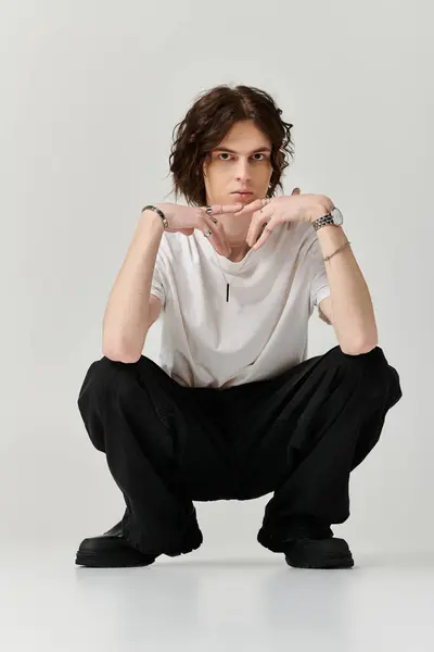 A handsome young man is squatting stylishly in a minimalistic studio, exuding confidence and charm. — Stock Photo