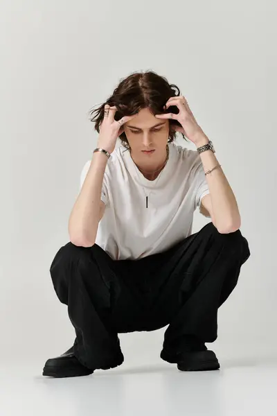 A handsome young man crouches thoughtfully, dressed in casual attire, reflecting a stylish vibe. — Stock Photo
