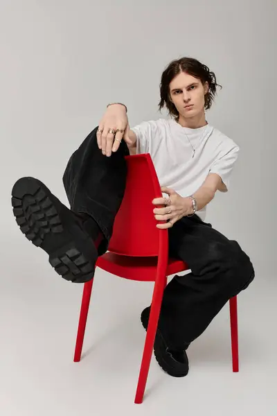 Young man in casual attire relaxes on a red chair, exuding confidence and style in a modern space. — Stock Photo