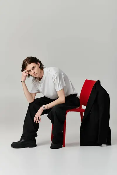A young man with a stylish look sits thoughtfully on a red chair in a contemporary studio space. — Stock Photo