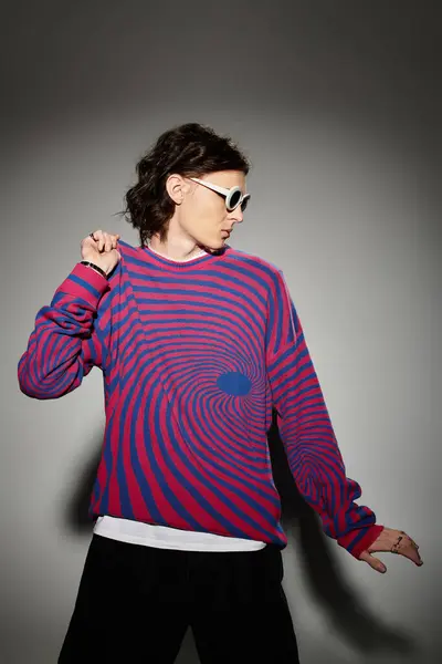Ein stilvoller junger Mann posiert verspielt in einem lebhaft gestreiften Pullover und einer Sonnenbrille. — Stockfoto