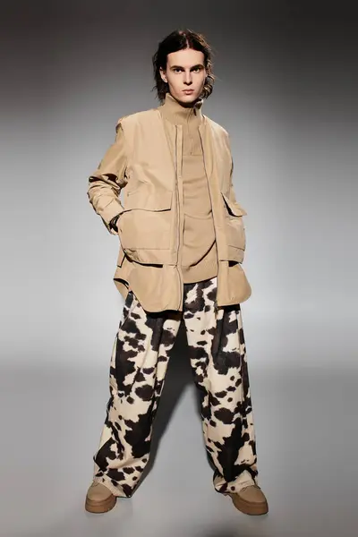 A stylish young man stands confidently in unique patterned, earthy toned attire. — Stock Photo